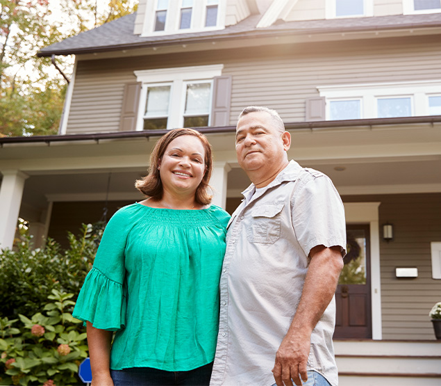 Smiling couple posing in front of their house.
